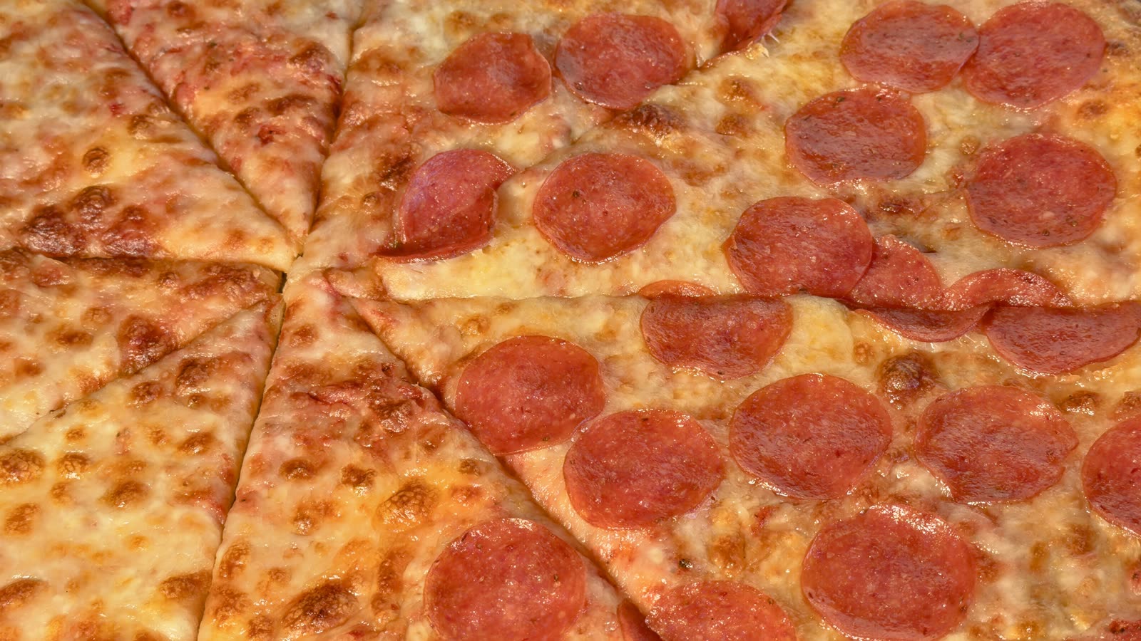 Close-up of freshly baked cheese and pepperoni pizzas cut into slices
