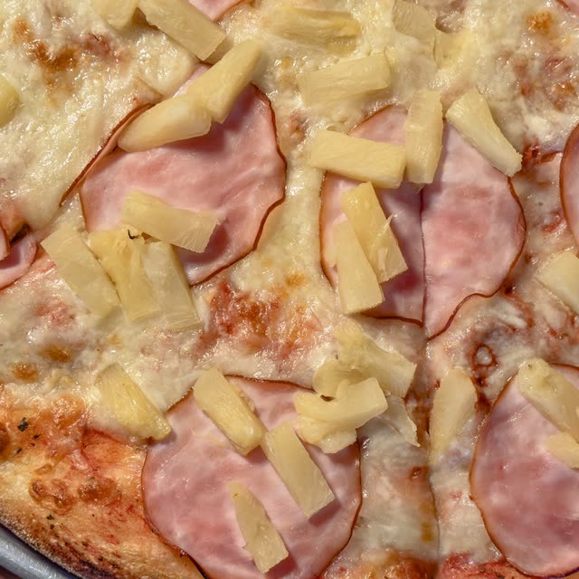 Leo pizza topped with Canadian bacon and pineapple chunks on melted mozzarella